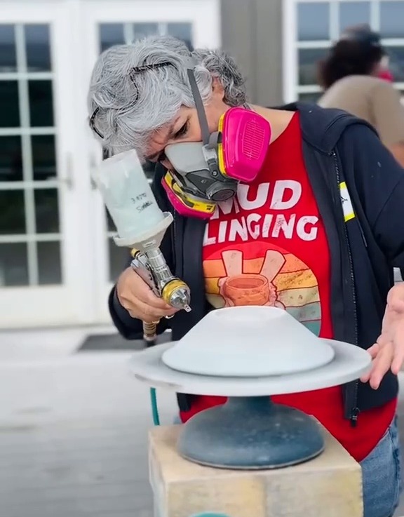 Maria spray-glazing a piece outdoors