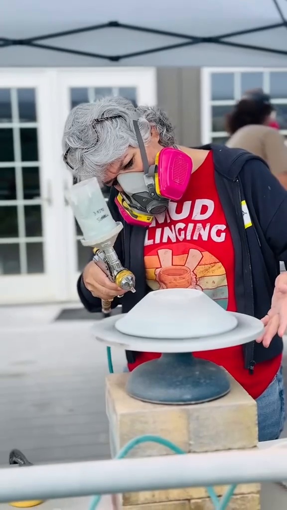 Maria spray-glazing a piece outdoors